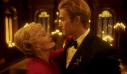 Due figure in una sala illuminata da luci dorate in American Horror Story 13x09