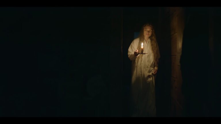 Giovane donna in camicia da notte bianca con una candela accesa in una stanza buia di East Of Eden 1x02